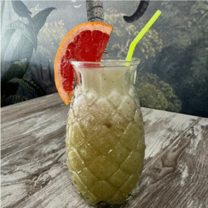 Cafetería Tanka's en Huelva: batido antioxidante verde con rodaja de pomelo y pajita amarilla, servido en vaso de cristal tallado.