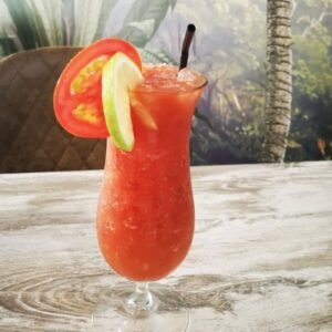 Vaso de Bloody Mary con hielo, limón y rodaja de tomate, servido sobre una mesa de madera