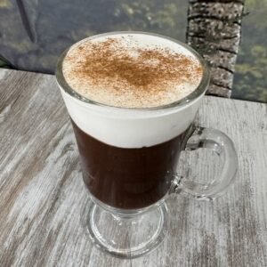 Taza de café brasileño con espuma de leche y canela, servida en vaso de cristal