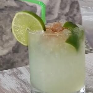 Caipirinha brasileña con hielo picado, rodajas de lima y canela, servida en vaso de cristal
