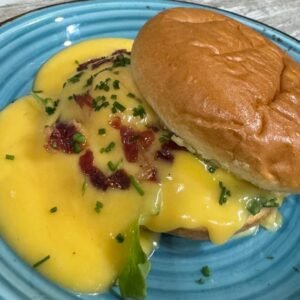 Huevo benedictino con salsa holandesa sobre panecillo, acompañado de cebollino y bacon crujiente