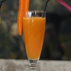 Zumo natural de naranja, zanahoria y jengibre servido en vaso con pajita