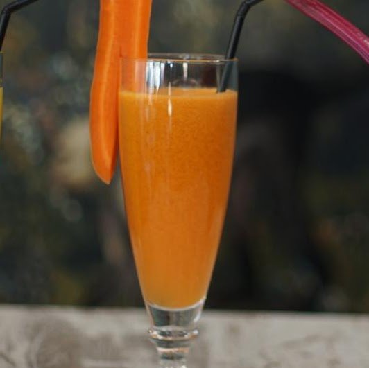 Zumo natural de naranja, zanahoria y jengibre servido en vaso con pajita