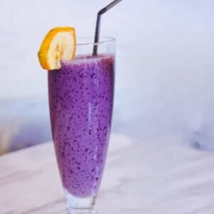Batido antioxidante de plátano y arándano servido en vaso alto con rodaja de plátano