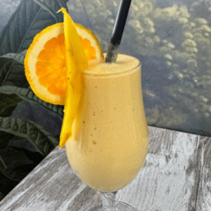 Batido tropical con rodaja de naranja y trozo de mango en vaso de cóctel