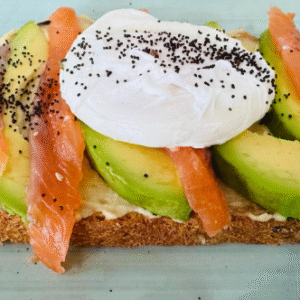 Tostada de pan rústico con aguacate, salmón ahumado y huevo poché, decorada con semillas de amapola