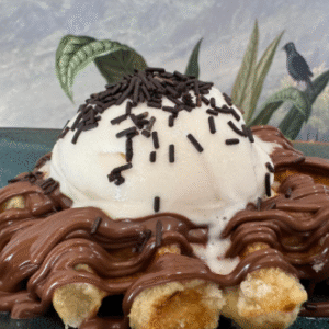 Gofre con bola de helado de vainilla, sirope de chocolate y virutas de chocolate, servido sobre plato azul